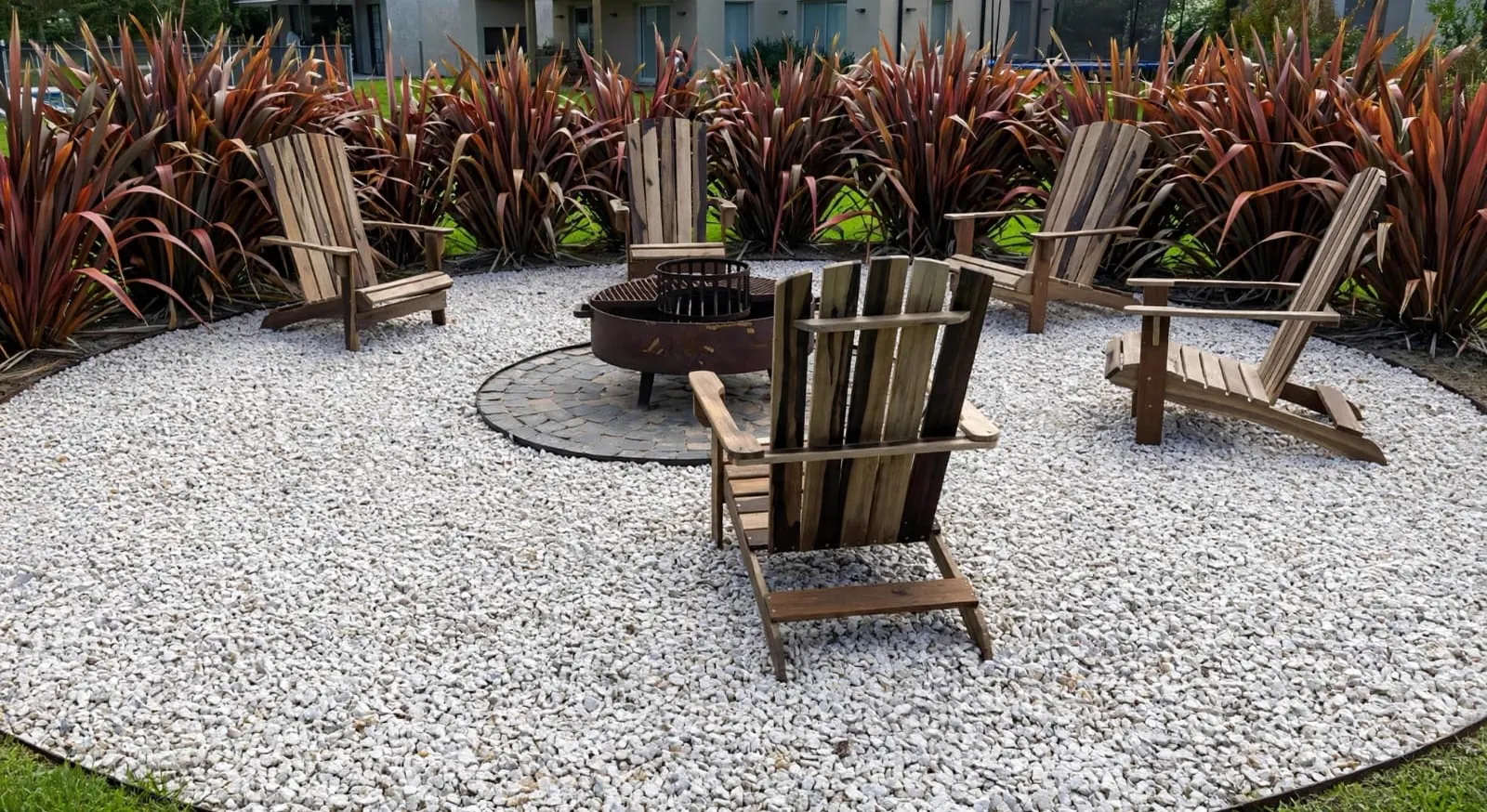 Sillones Adirondack de madera en ronda alrededor de un fogón, en un jardín
